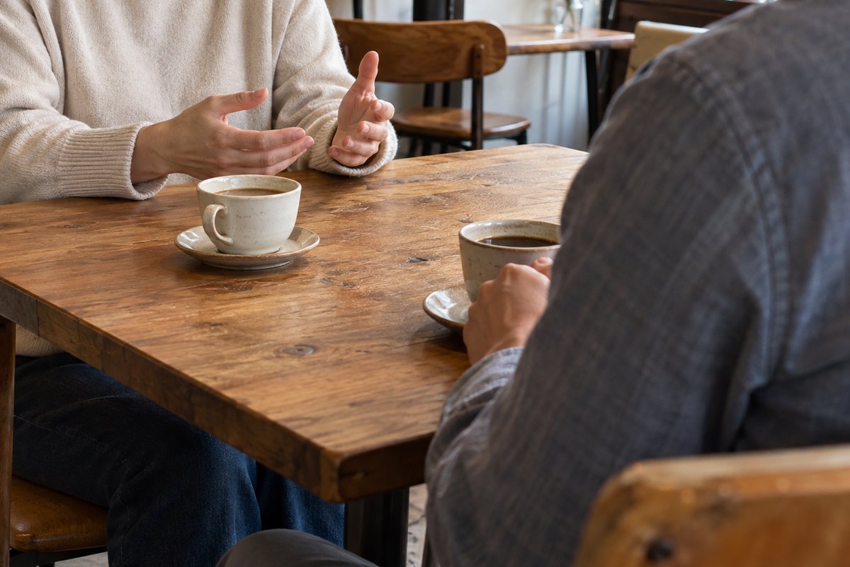英会話カフェで話す様子をイメージした写真。テーブルでコーヒーを前に向かい合って話す2人